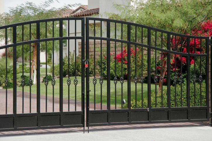 A black wrought iron gate is open in front of a house.
