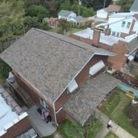 Brown-roofed brick house viewed from above, surrounded by trees and other buildings in a residential area.