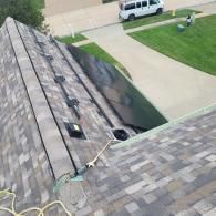 A roof with gray shingles, including vents and flashing, with a nearby van and grass.