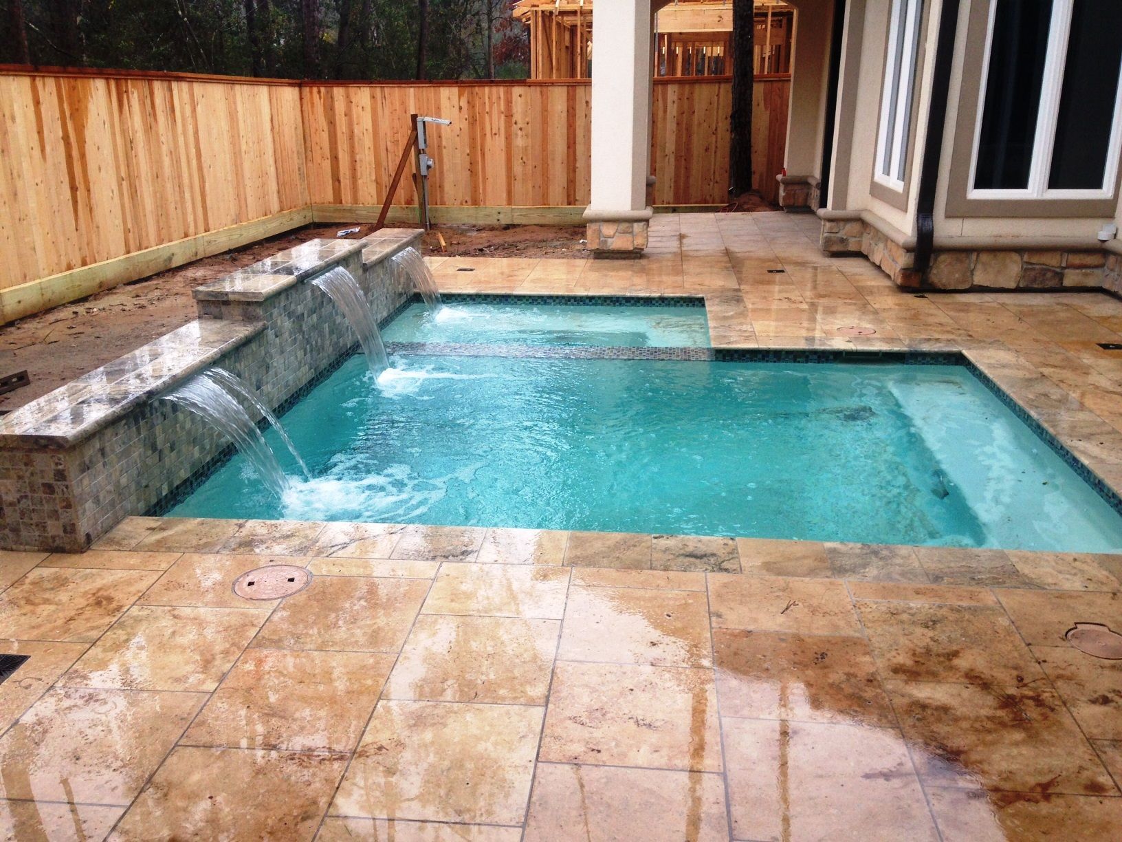 A large swimming pool with a waterfall in the backyard of a house.
