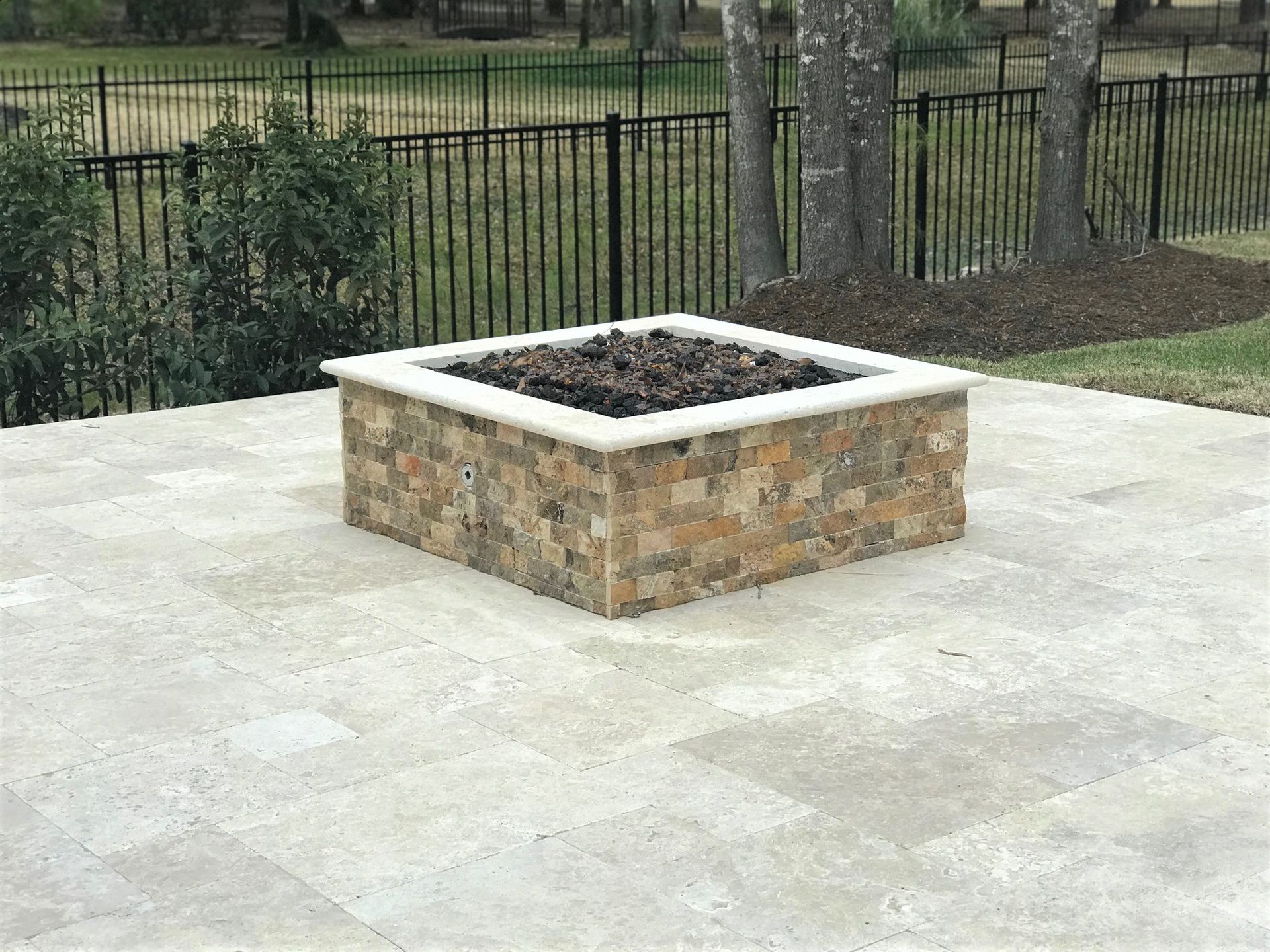 A fire pit is sitting on a patio next to a fence.