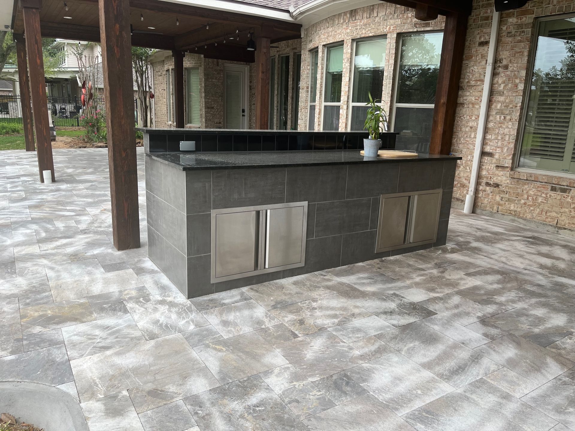 A large outdoor kitchen is sitting on a patio next to a brick house.