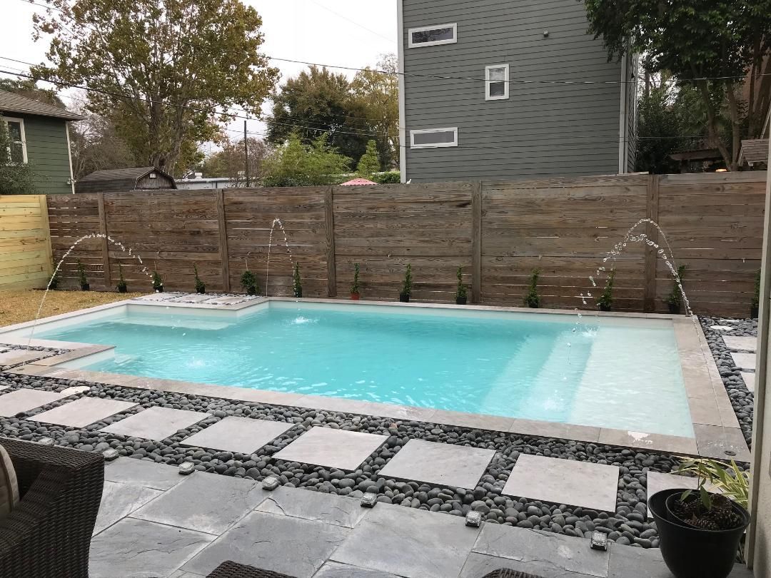 A large swimming pool with a fountain in the backyard of a house.