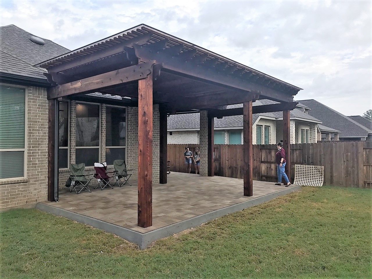 A man and a child are standing under a wooden pergola in the backyard of a house.