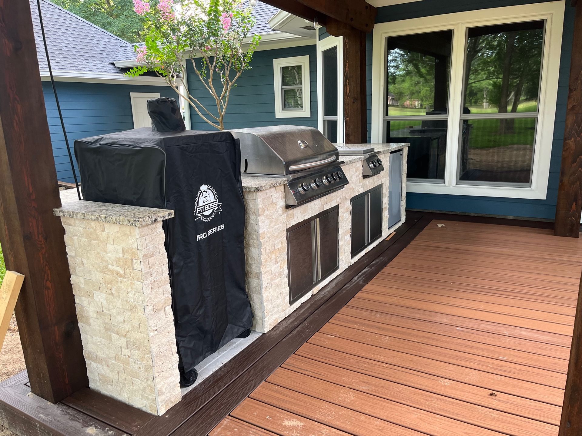A grill is sitting on a wooden deck next to a blue house.