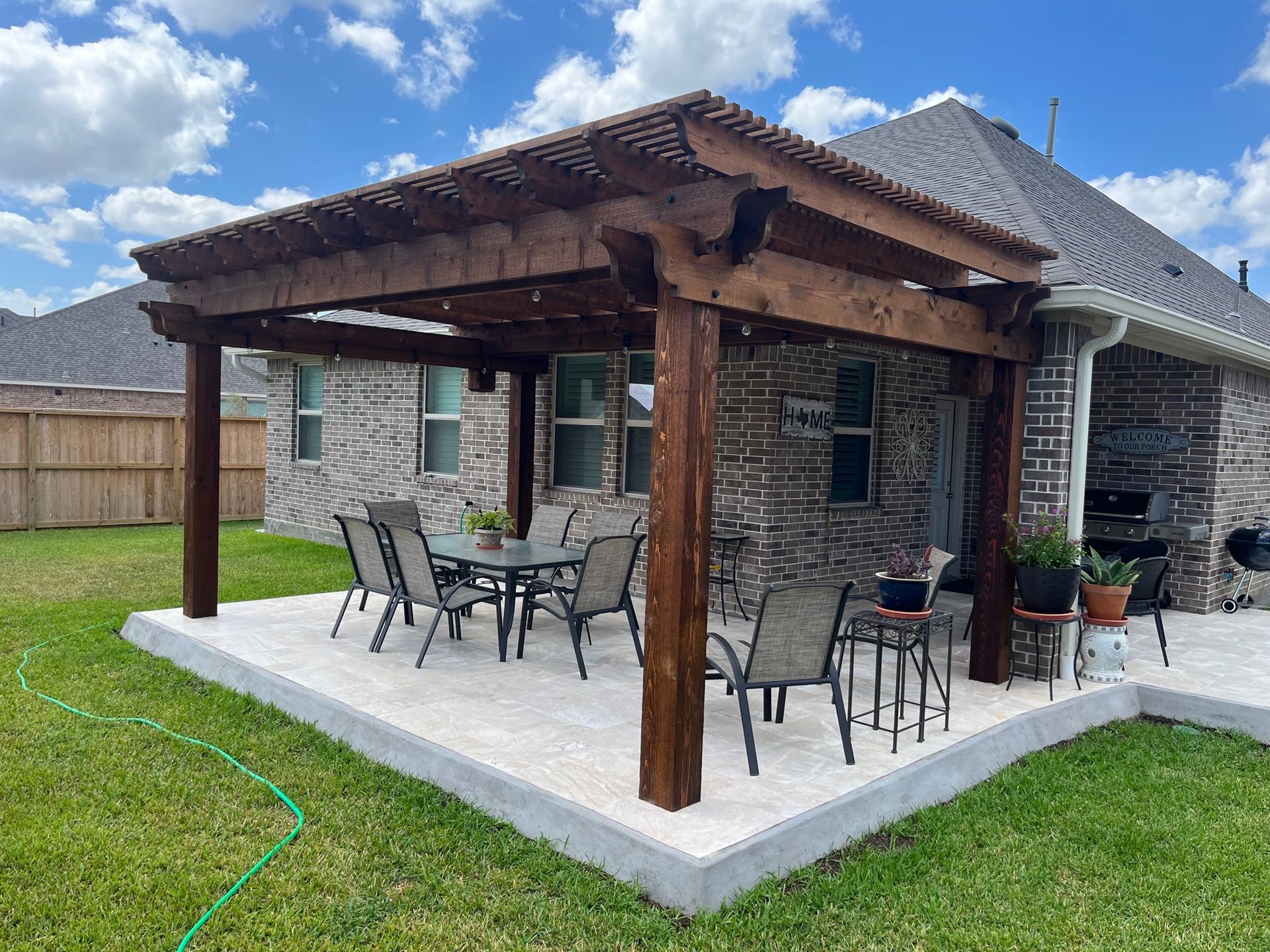 A wooden pergola with a table and chairs is in the backyard of a house.