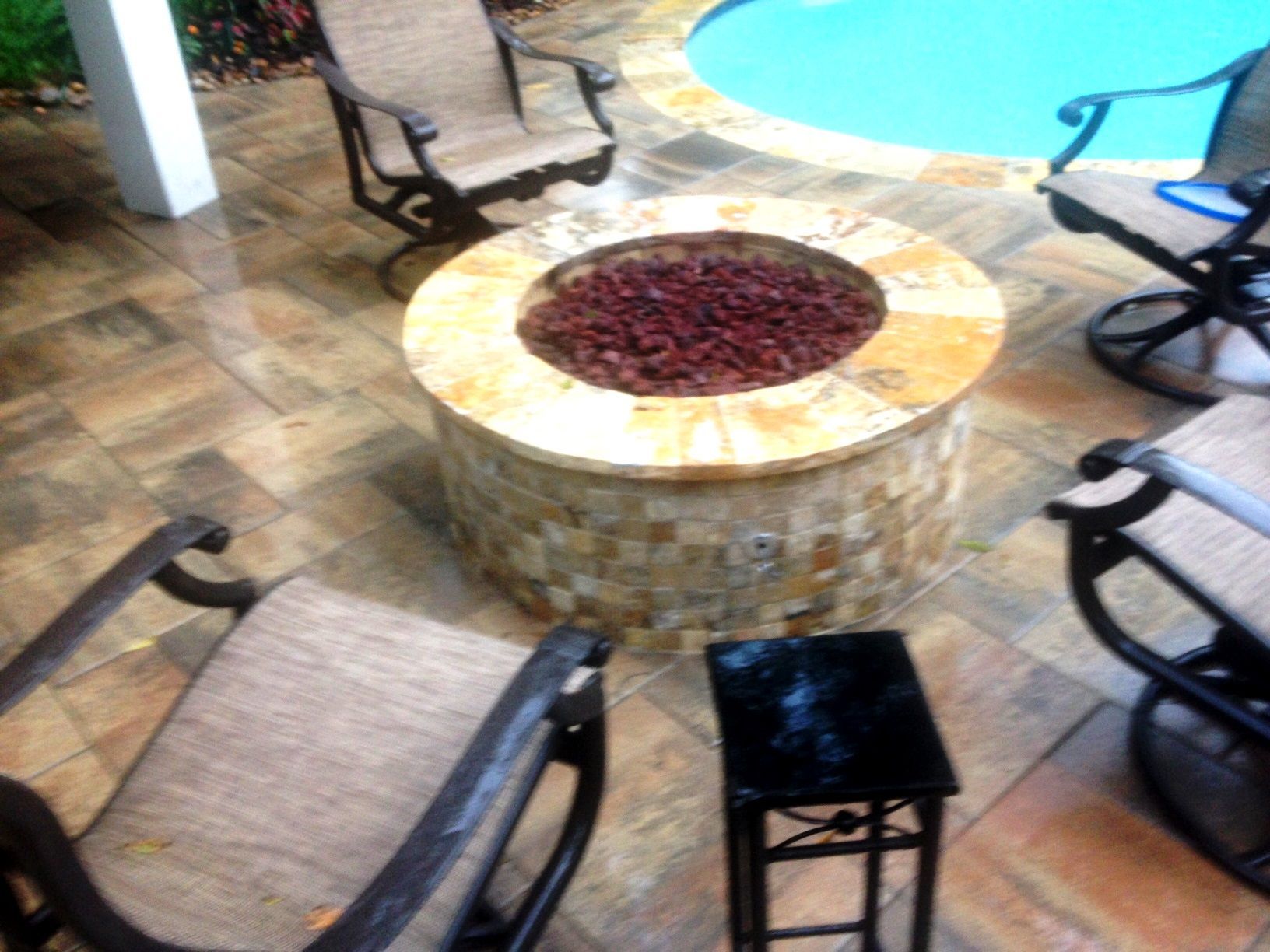 A fire pit sits on a patio next to a pool