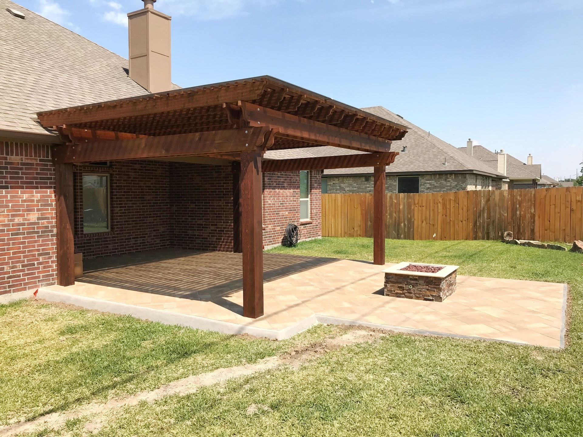 A wooden pergola with a fire pit in the backyard of a house.