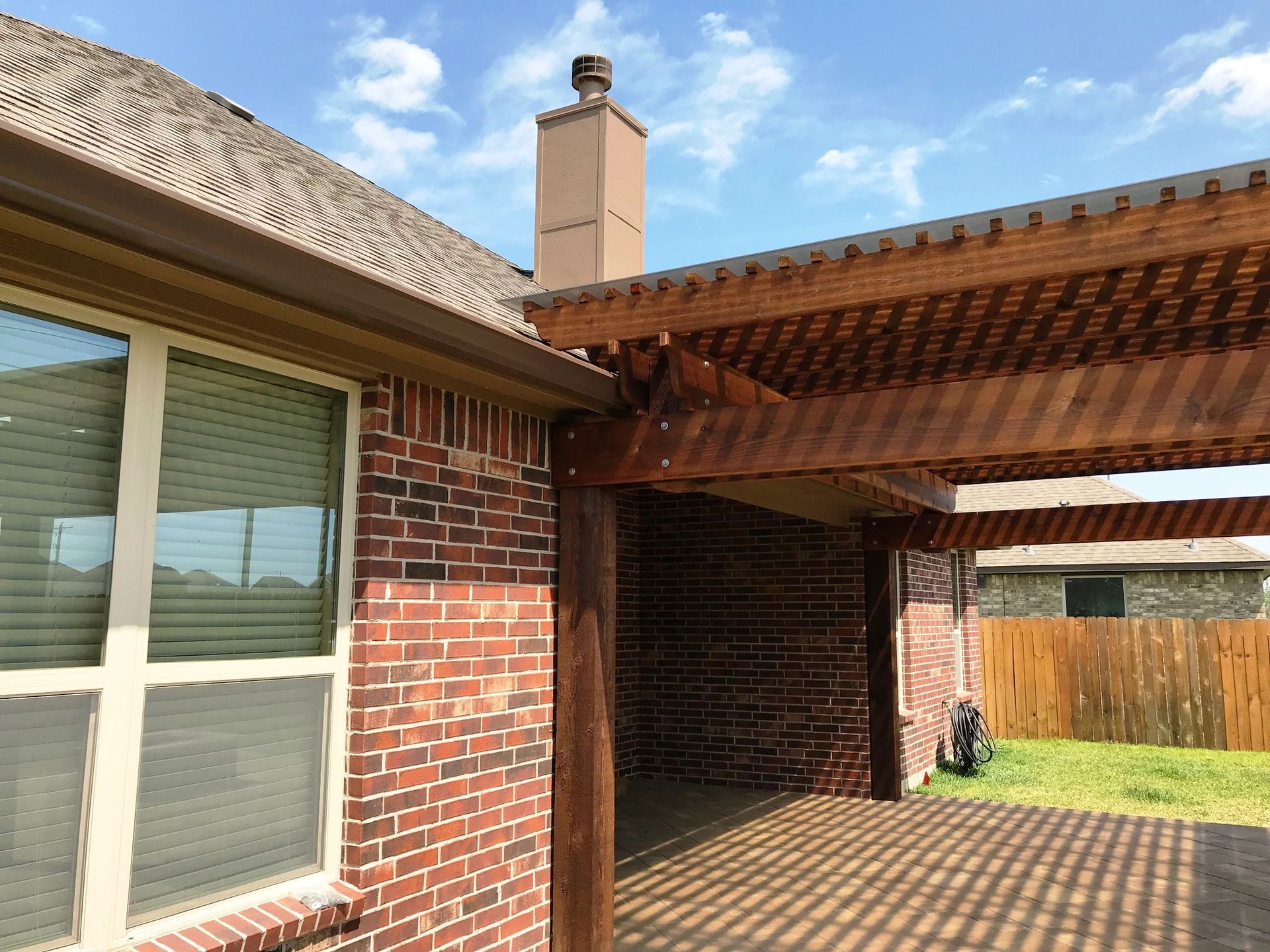 A brick house with a wooden pergola on the side of it.