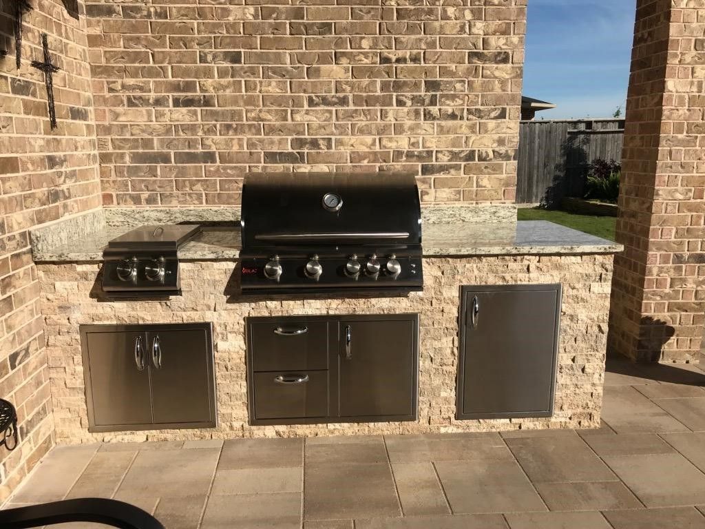 An outdoor kitchen with a grill and stainless steel cabinets
