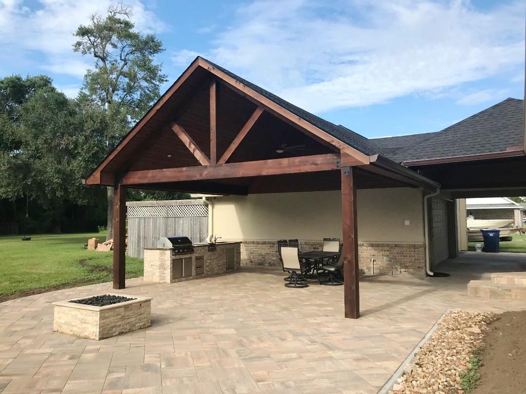 A wooden pavilion with a grill and a fire pit in front of a house.