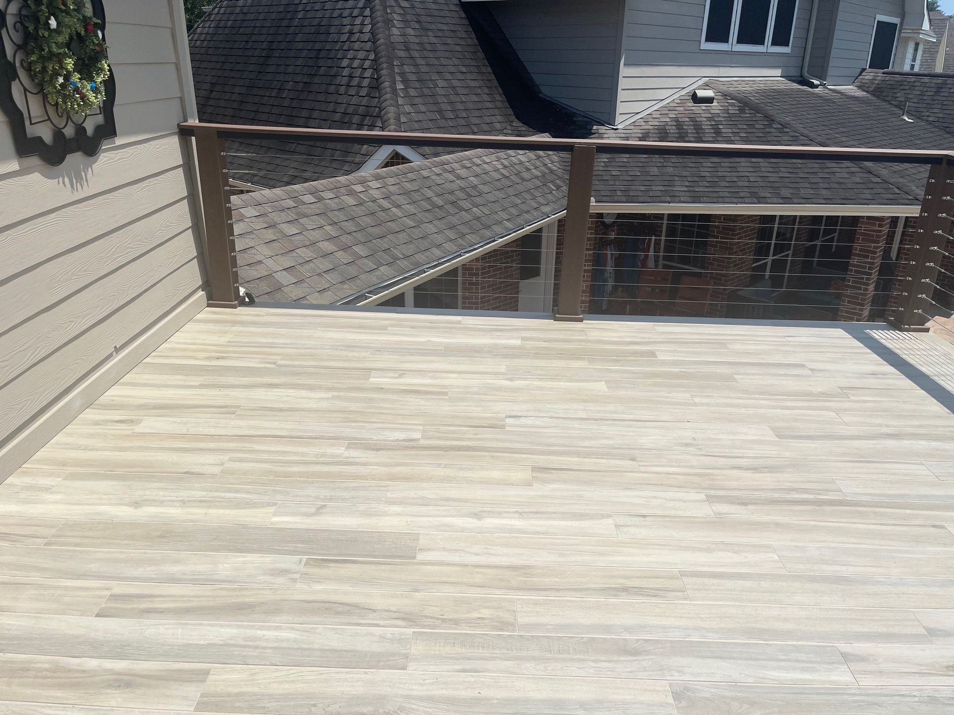 A wooden deck with a glass railing and a view of a house.