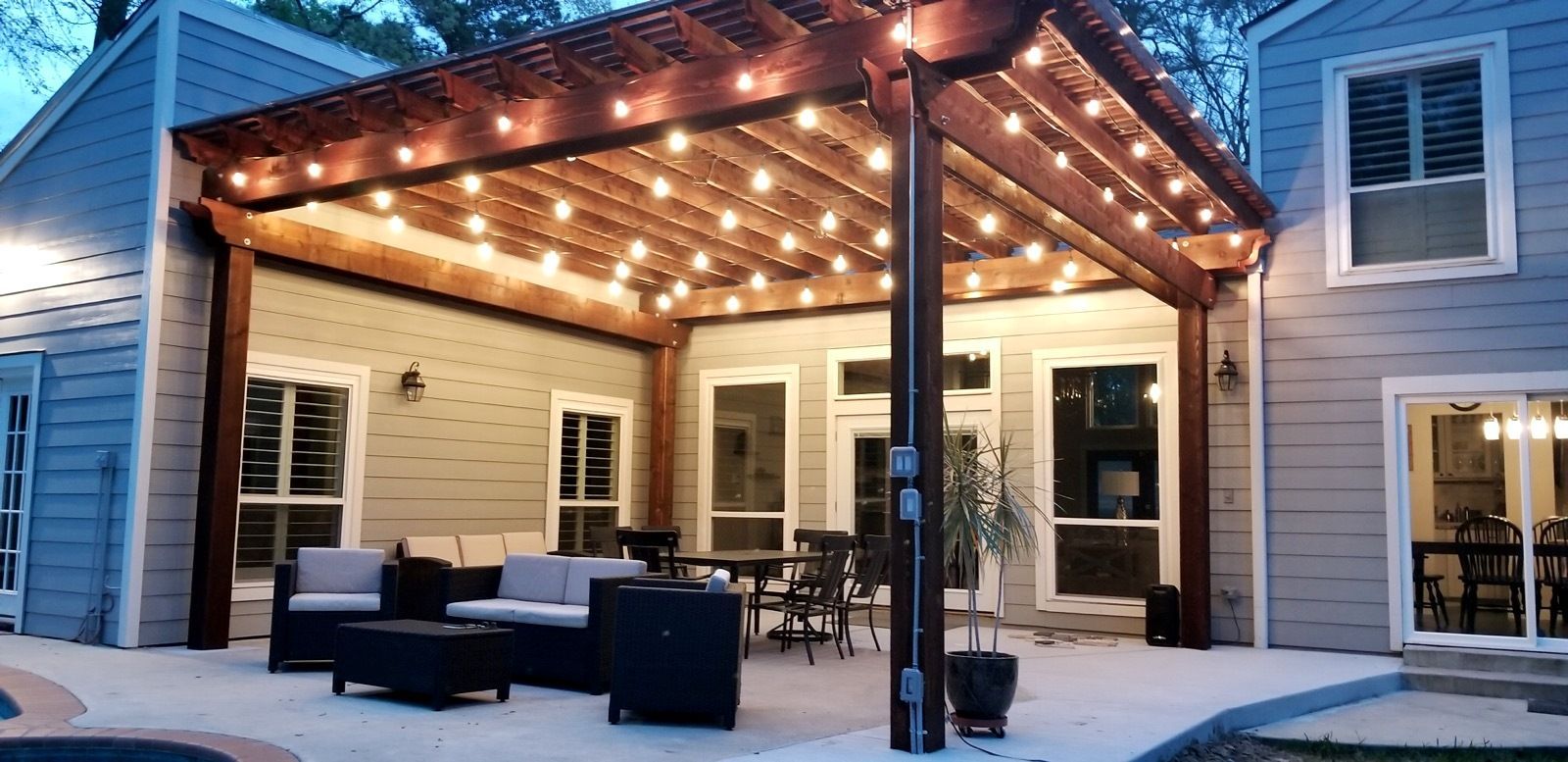A patio with a pergola and string lights is lit up at night.
