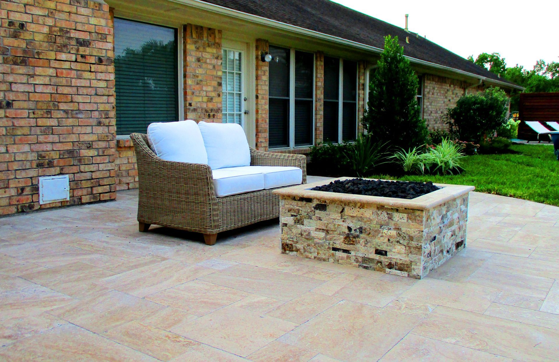 A patio with a couch and a fire pit in front of a brick house