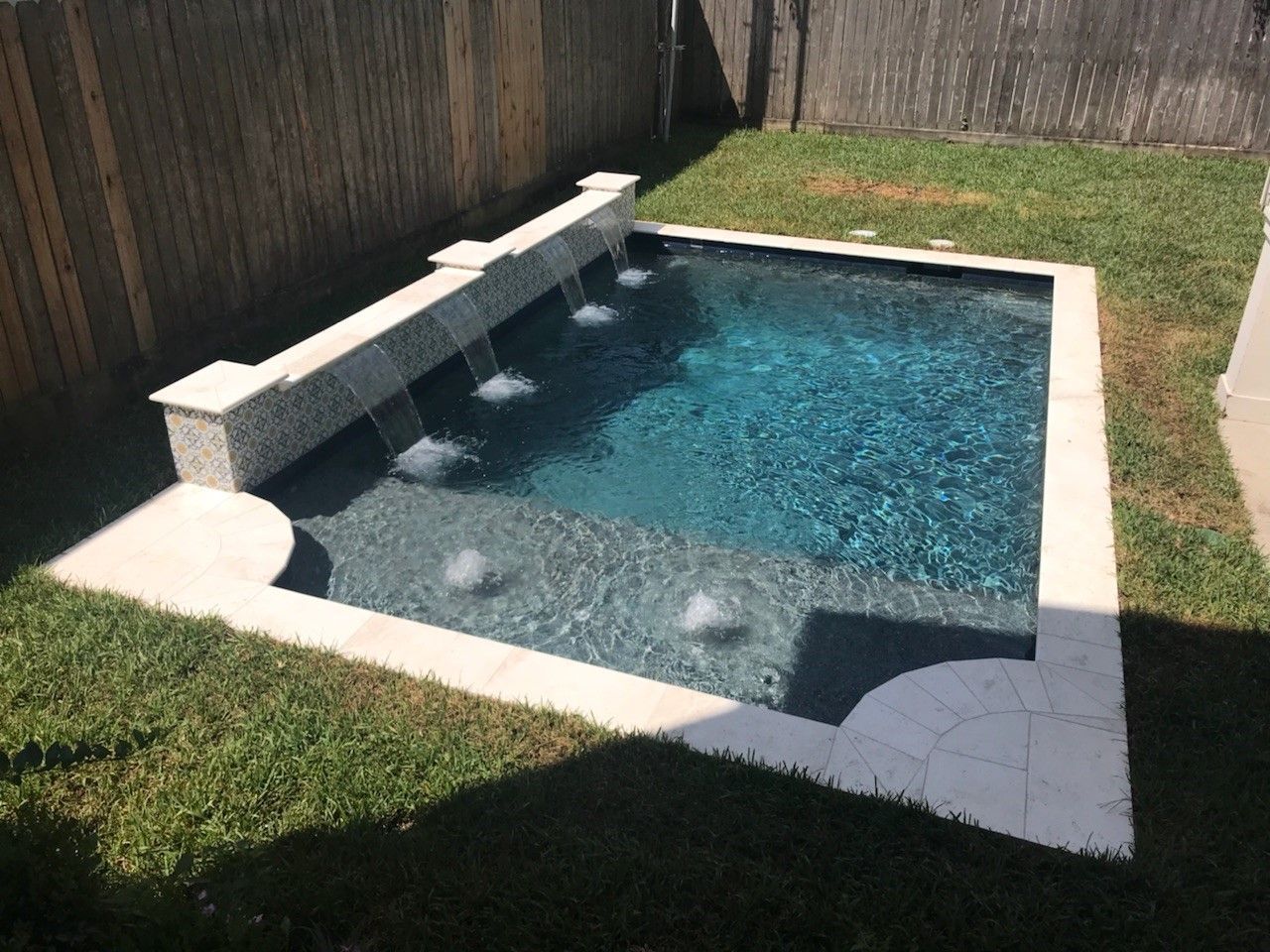 A small swimming pool with a waterfall in the backyard.