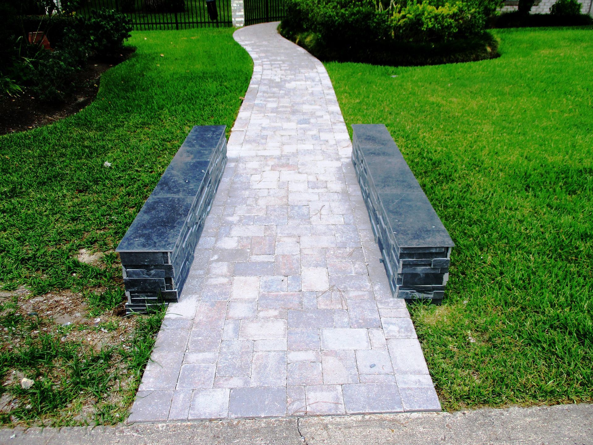 A brick walkway going through a lush green lawn