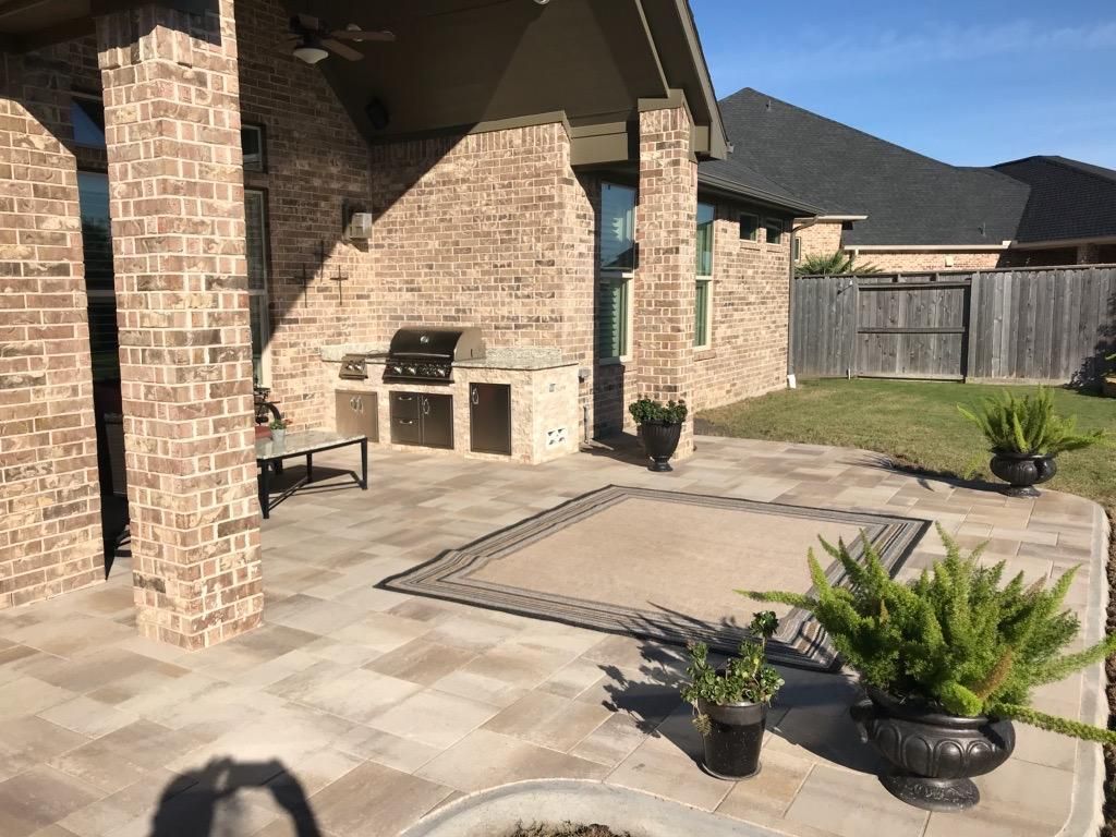 A patio with a grill and potted plants in front of a brick house.