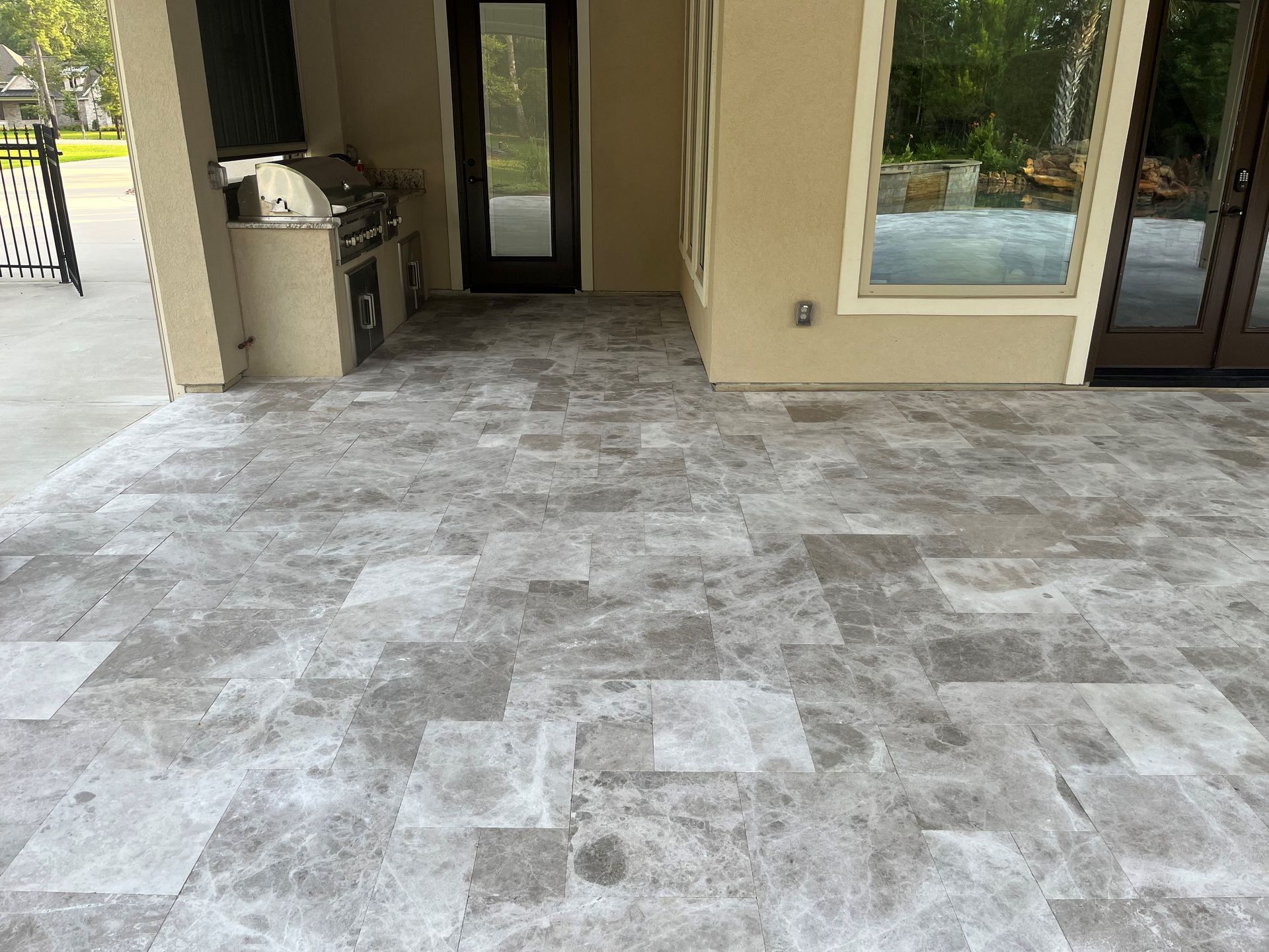 A patio with a tiled floor and a grill in the background.