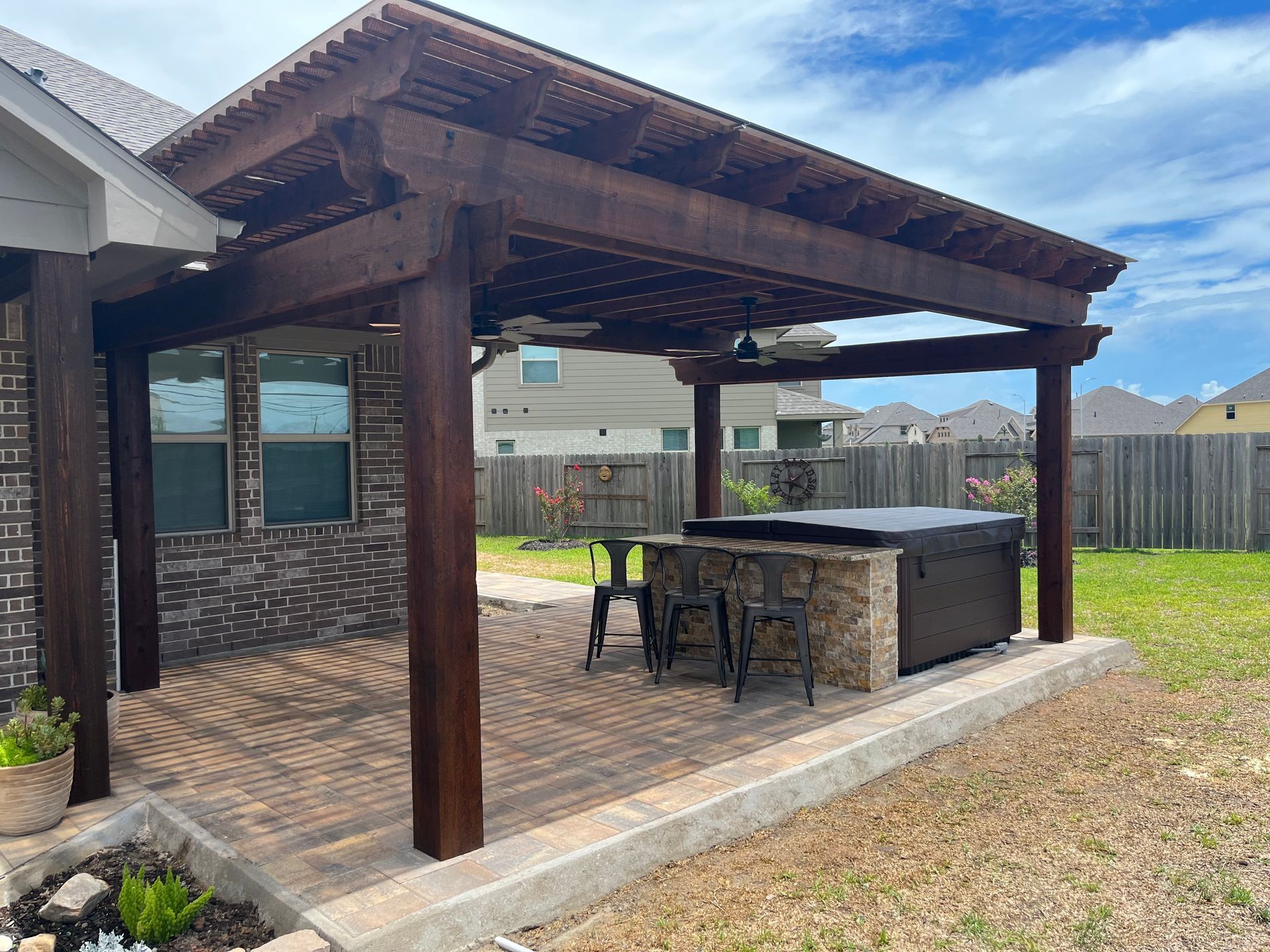 A wooden pergola with a hot tub underneath it in a backyard.