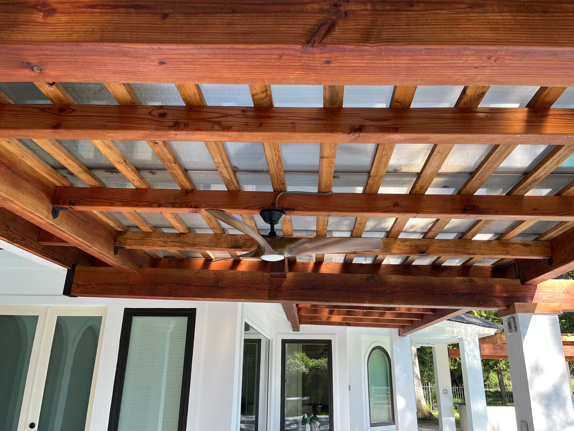 A ceiling fan is hanging from the ceiling of a wooden pergola.