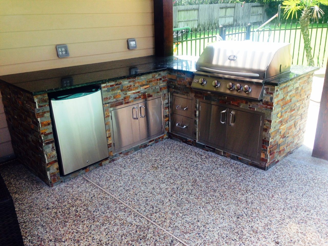 An outdoor kitchen with a grill and a refrigerator