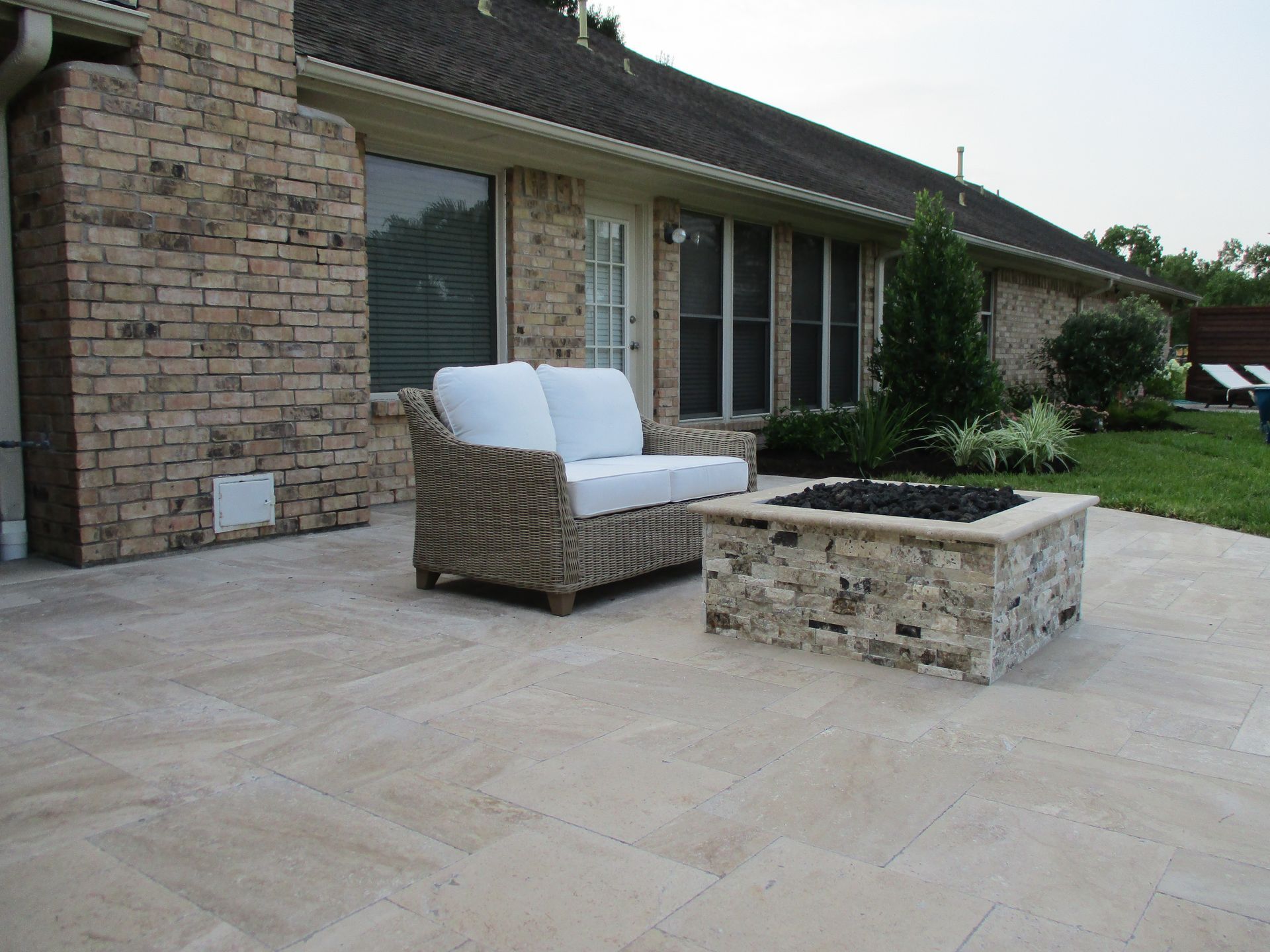 A patio with a fire pit and a couch in front of a brick house