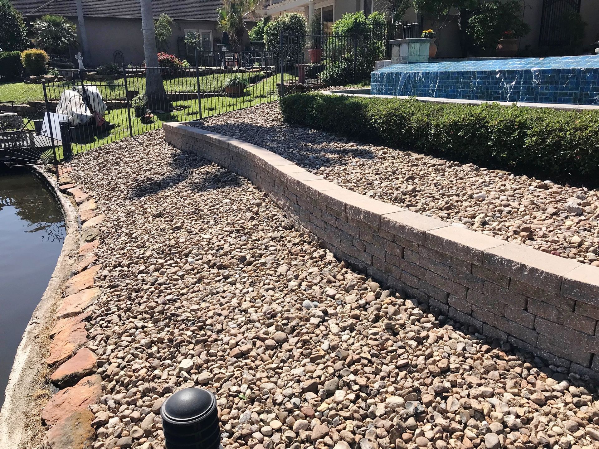 A brick wall is surrounded by gravel next to a pool.
