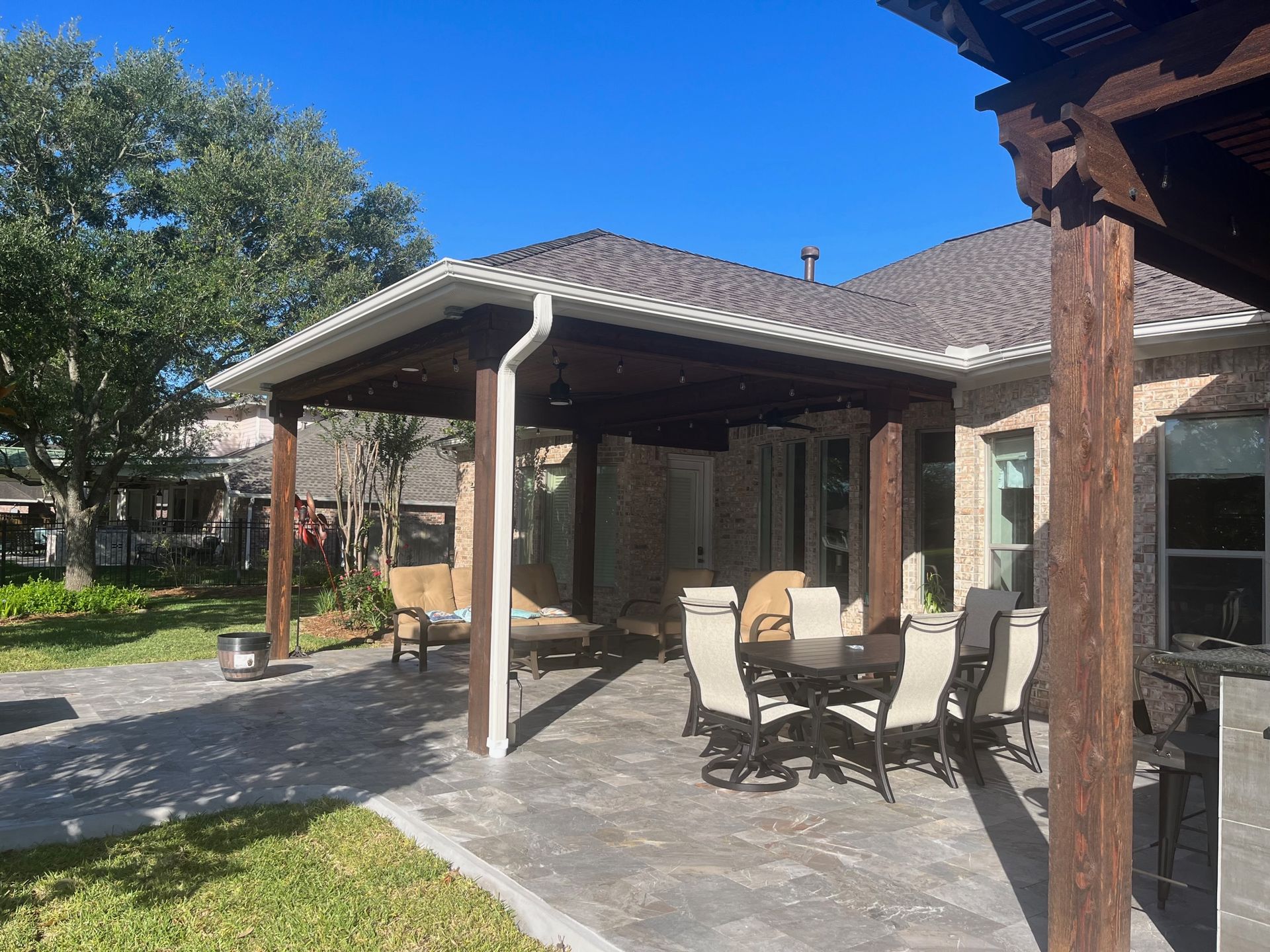 A patio with a table and chairs under a pergola in front of a house.