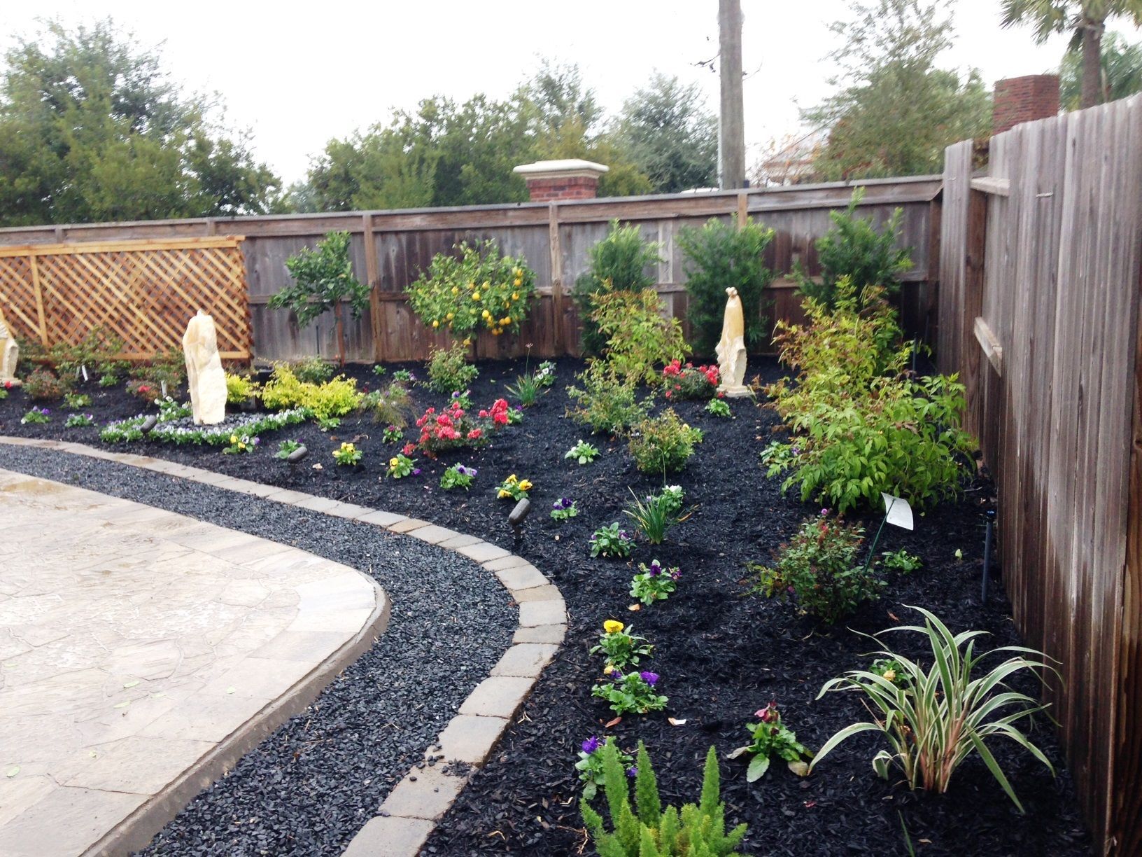 A garden with a wooden fence and black mulch