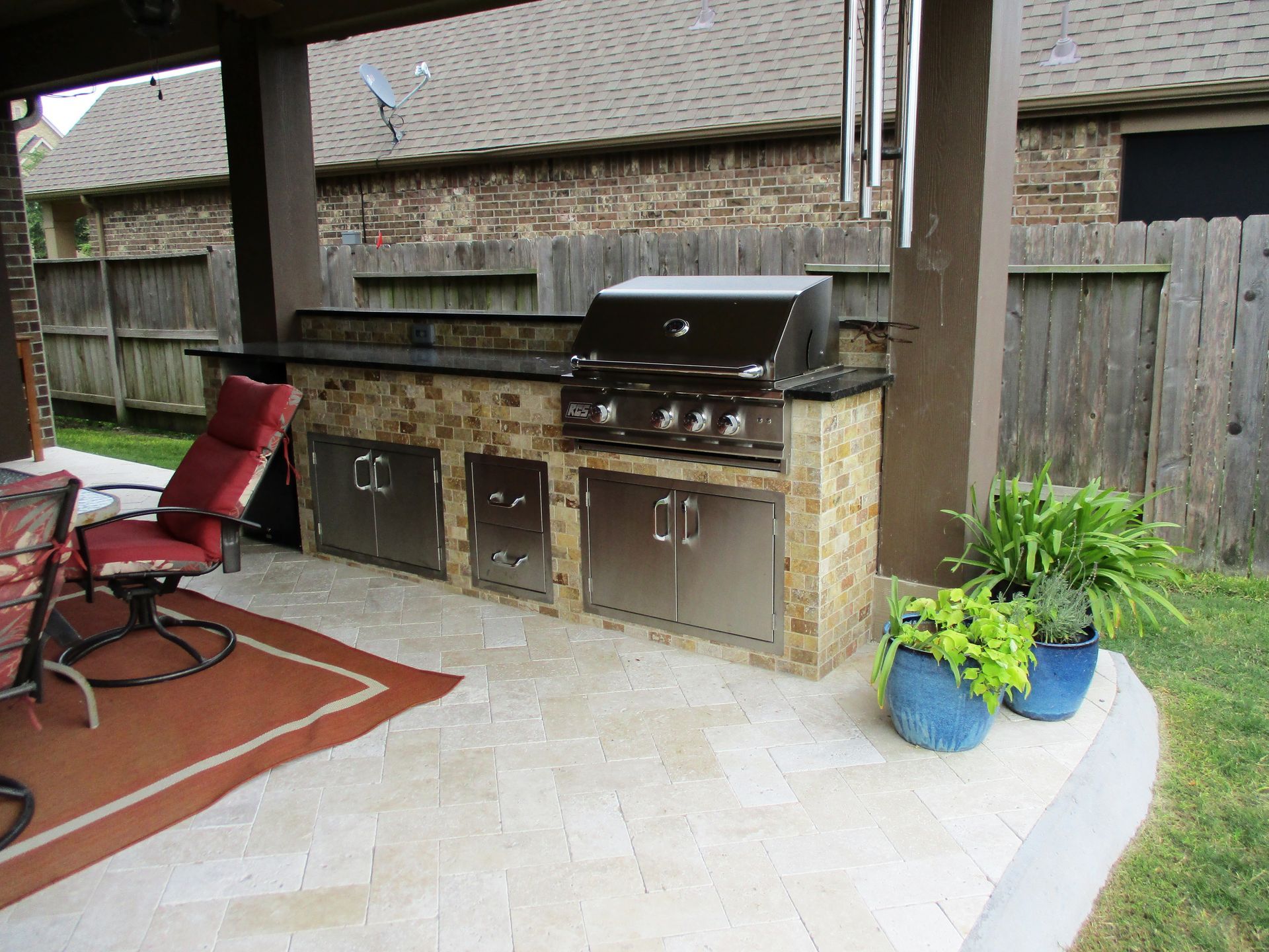 A patio with a grill , chairs , and potted plants.