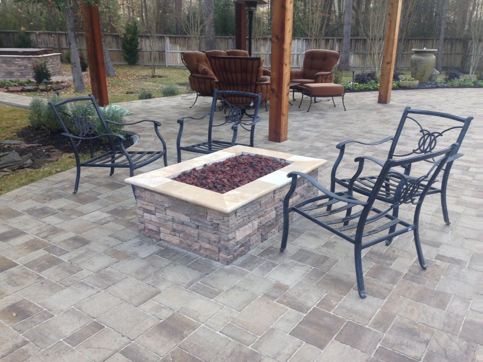 A fire pit on a patio with chairs and a pergola.
