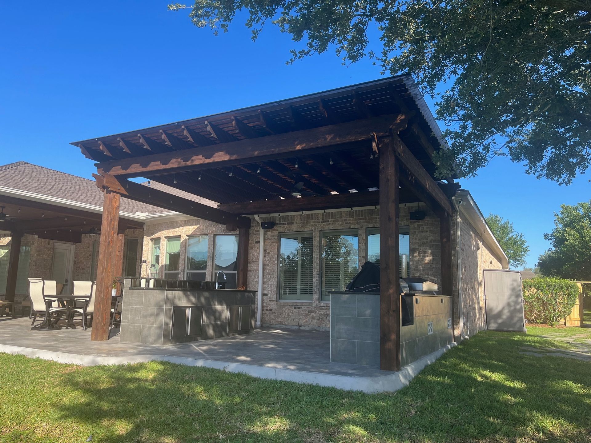A patio with a pergola and a grill in the backyard of a house.