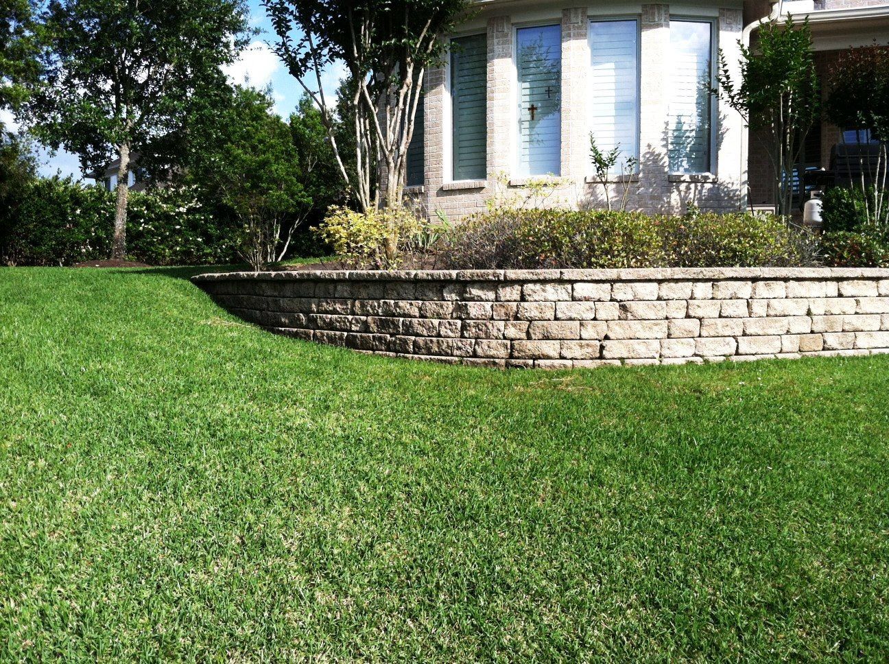 A lush green lawn in front of a house with a brick wall.