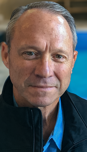 A close up of a man 's face wearing a blue shirt and a black jacket.