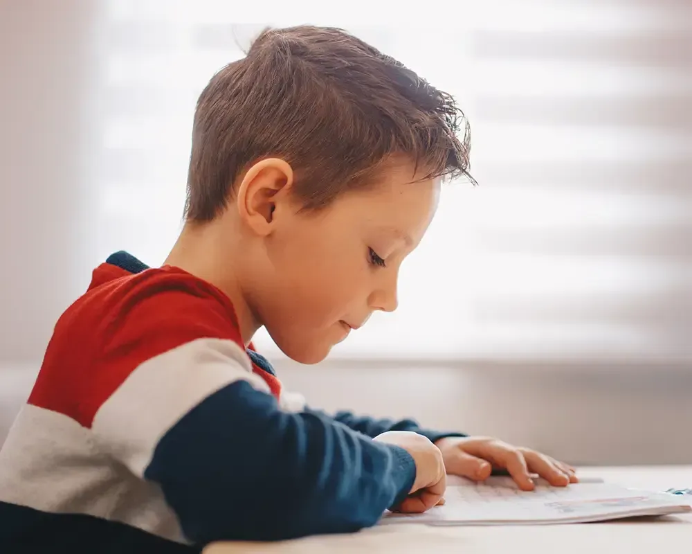 Un niño pequeño está sentado en una mesa leyendo un libro.