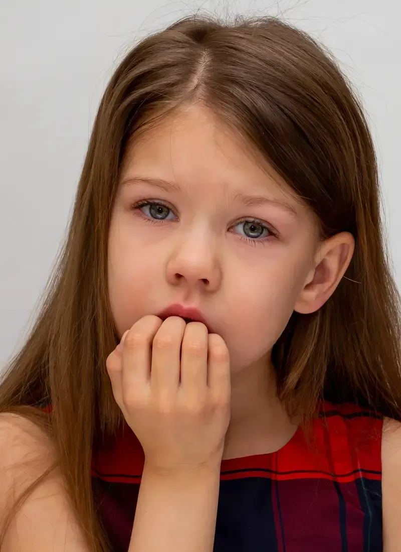 Una niña se muerde las uñas y mira a la cámara.