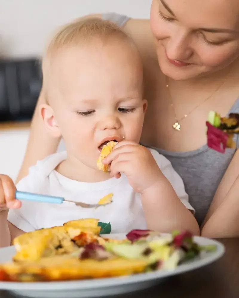 Una mujer está alimentando a un bebé con un plato de comida.