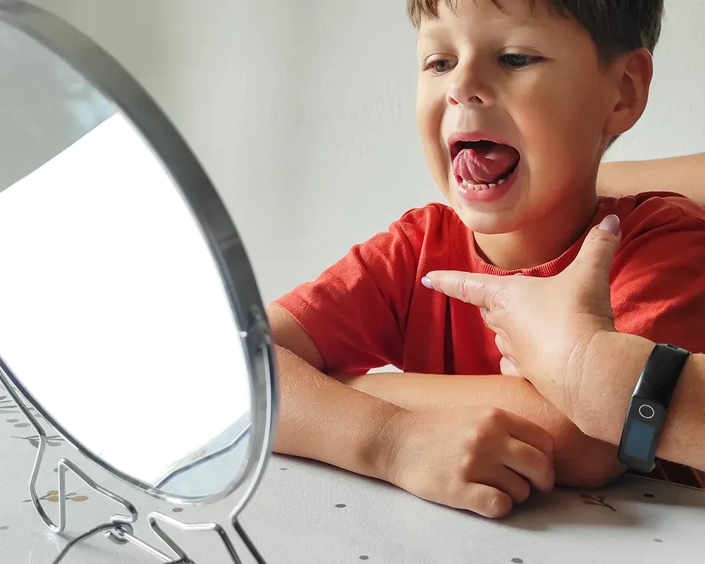 Un niño pequeño se mira la lengua en un espejo.