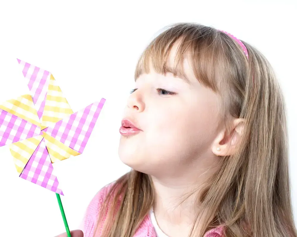 Una niña está soplando un molino de viento rosa y amarillo.