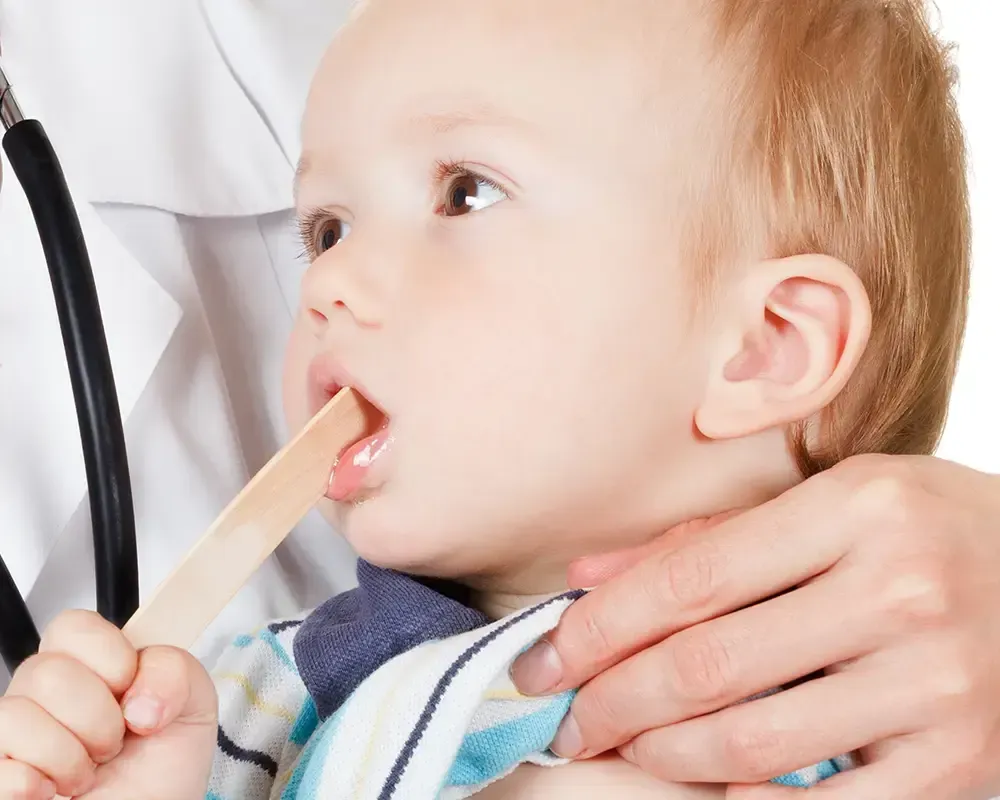 Un médico está examinando la garganta de un bebé con un depresor de lengua.