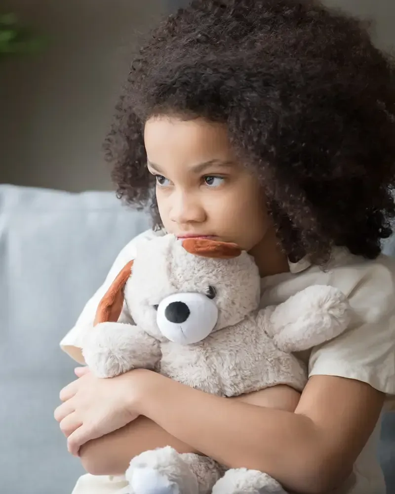 Una niña está sentada en un sofá sosteniendo un osito de peluche.