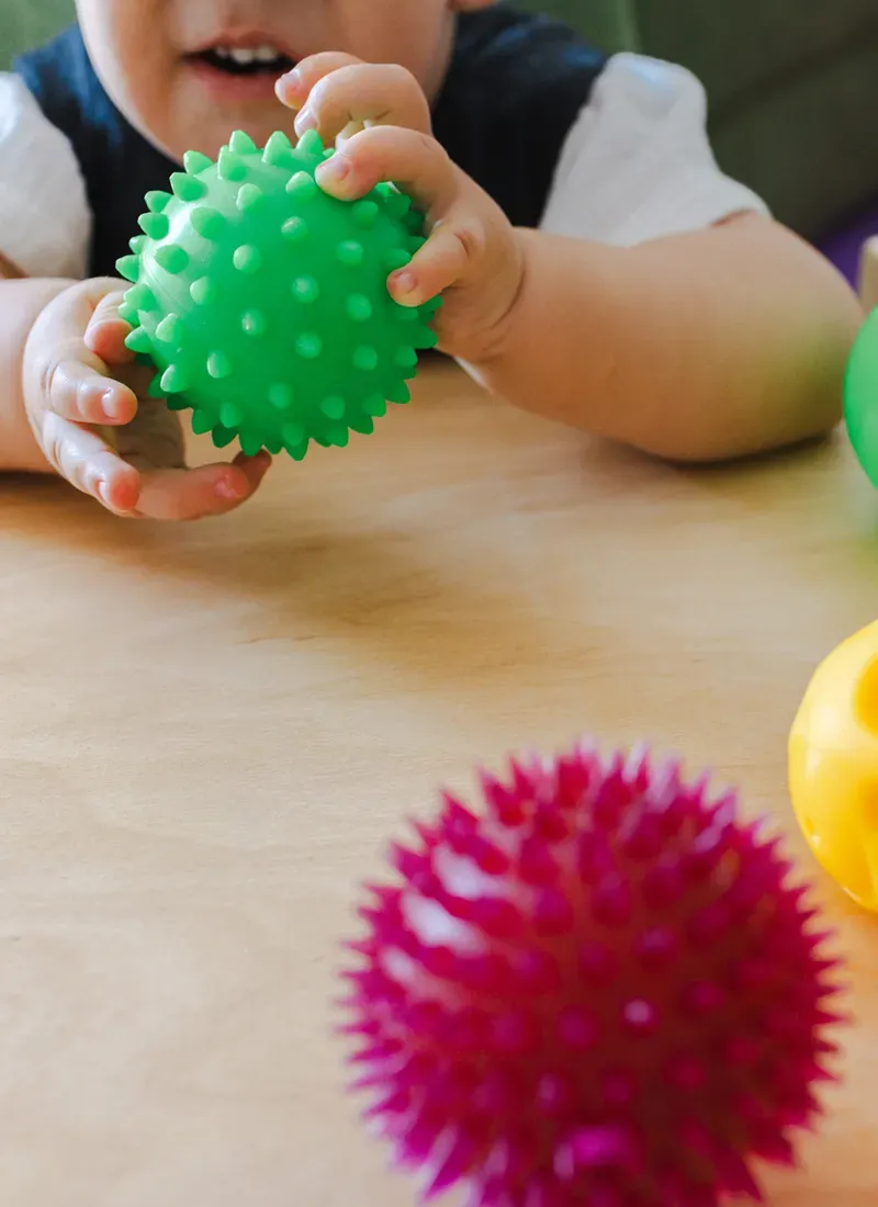 Un niño está jugando con una pelota verde sobre una mesa.