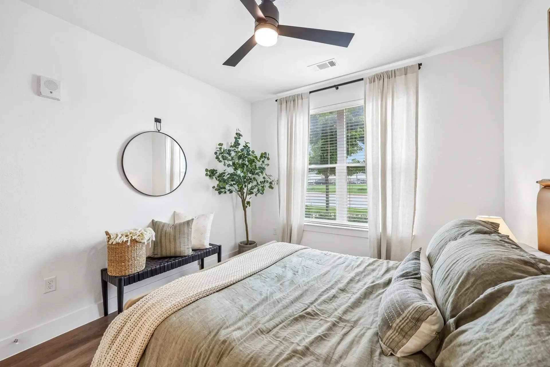 Bedroom with a king-size bed, white walls, a ceiling fan, and a window with sheer curtains.
