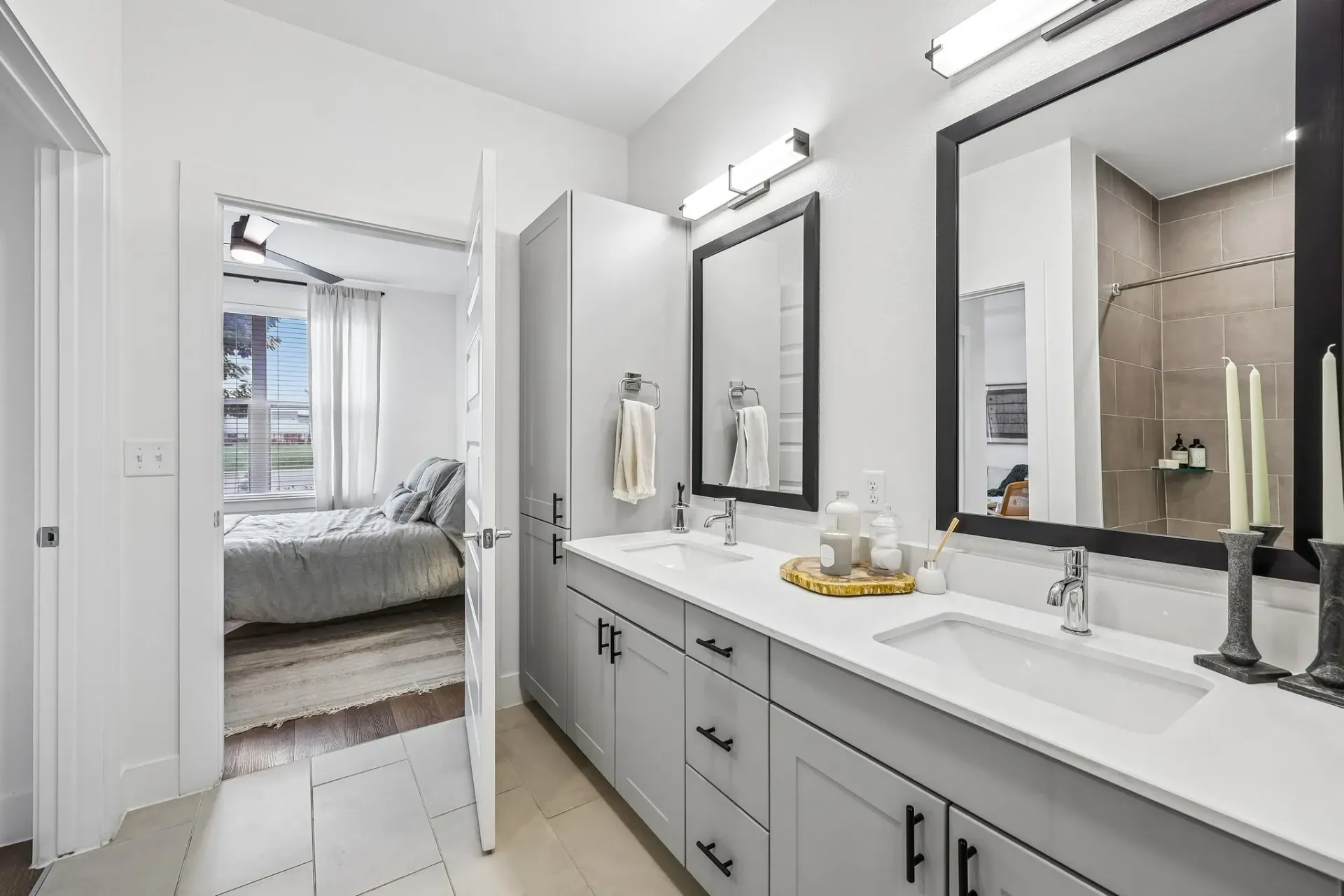 Modern bathroom with double vanity, large mirrors, and view into bedroom.