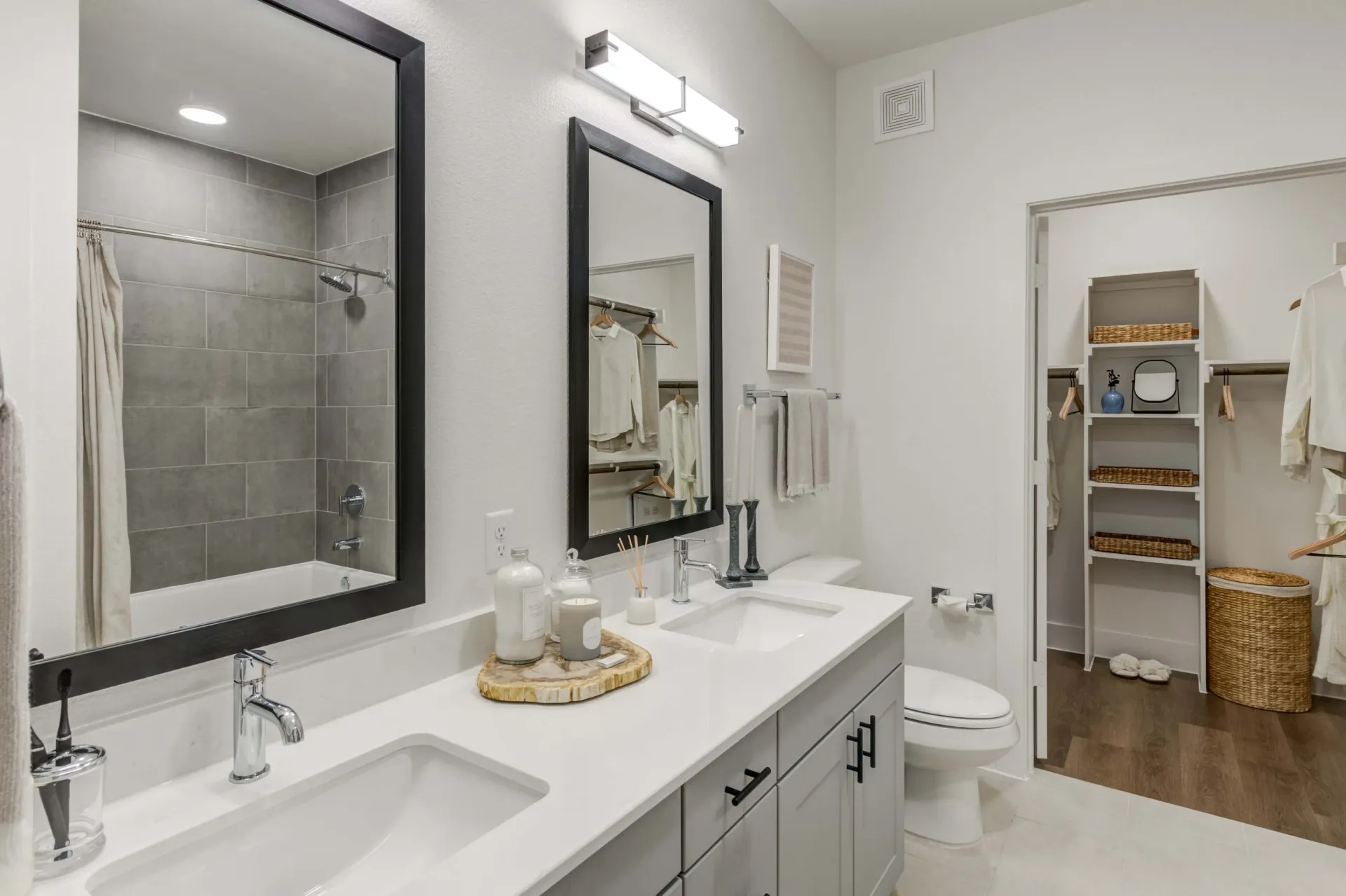 Modern bathroom with dual vanities, a bathtub with shower, and a walk-in closet.