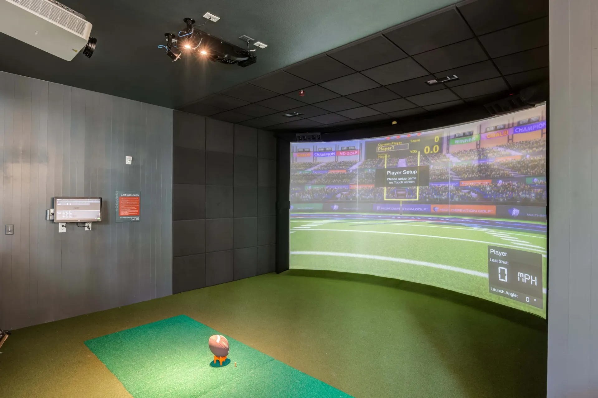 Indoor golf simulator with a large curved screen displaying a football stadium.