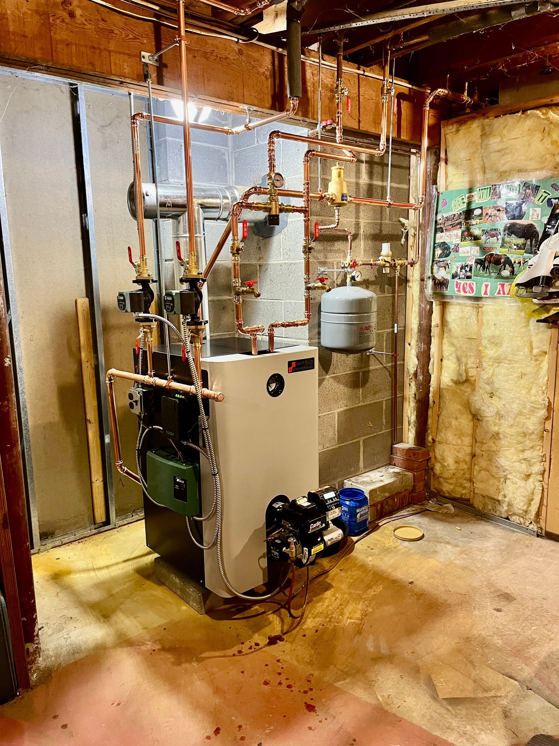 Boiler with copper piping in a basement. Grey furnace, white expansion tank, blue pump, and exposed block wall.
