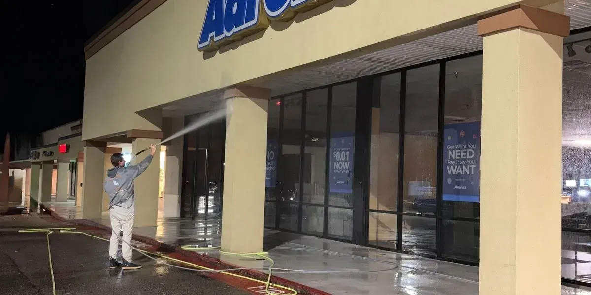 Person washing windows outside a storefront at night, with a squeegee and water spray.