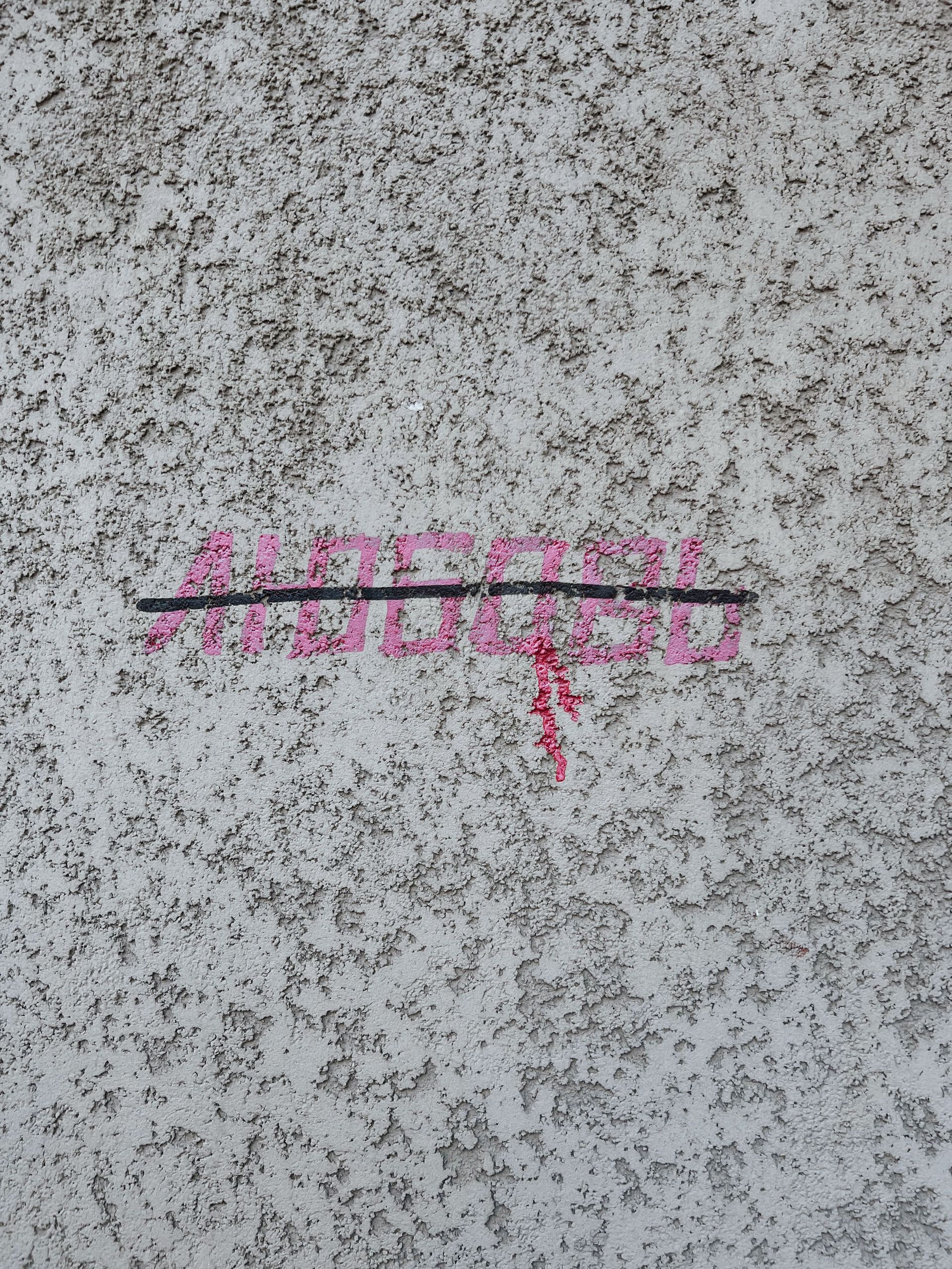 Pink graffiti tag and black line on a speckled gray concrete surface