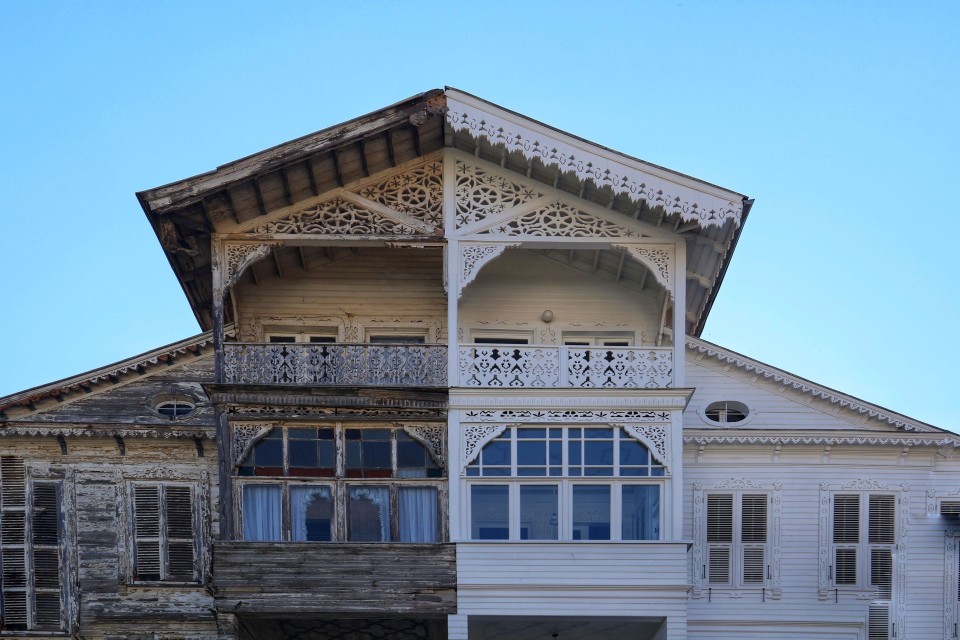 Ornate historic house facade with white and weathered wood trim under a blue sky